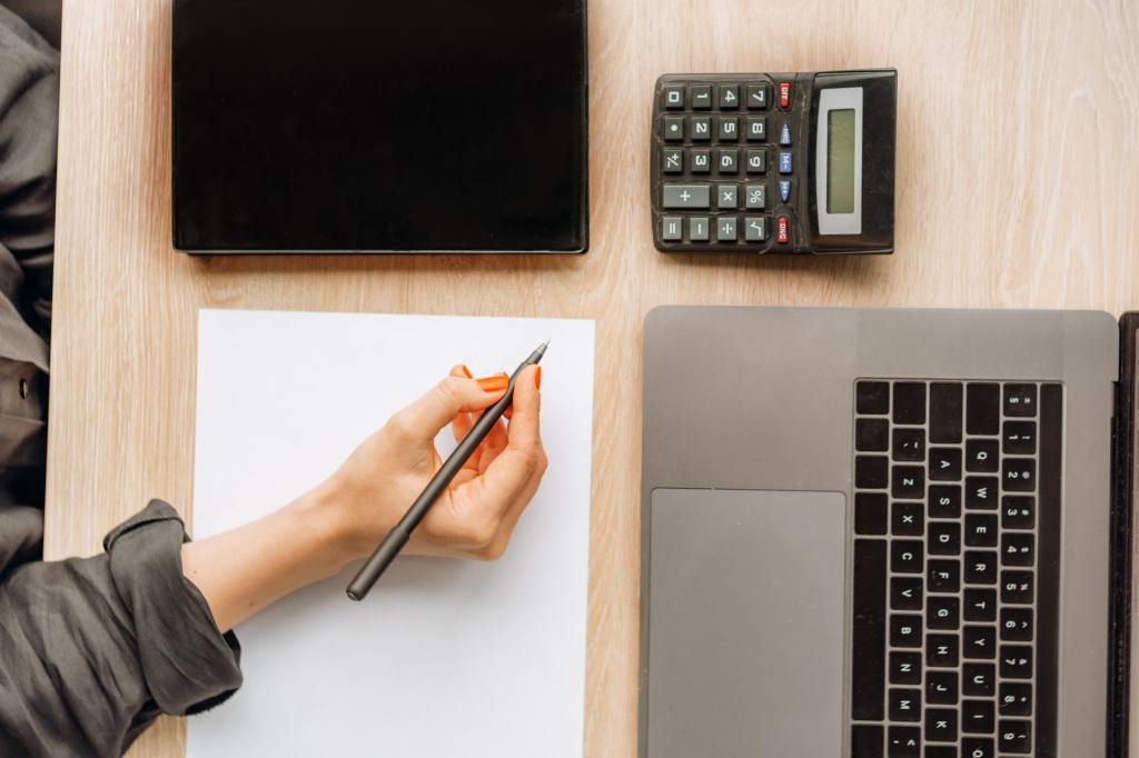 woman-taking-notes-with-laptop-calculator-and-tablet